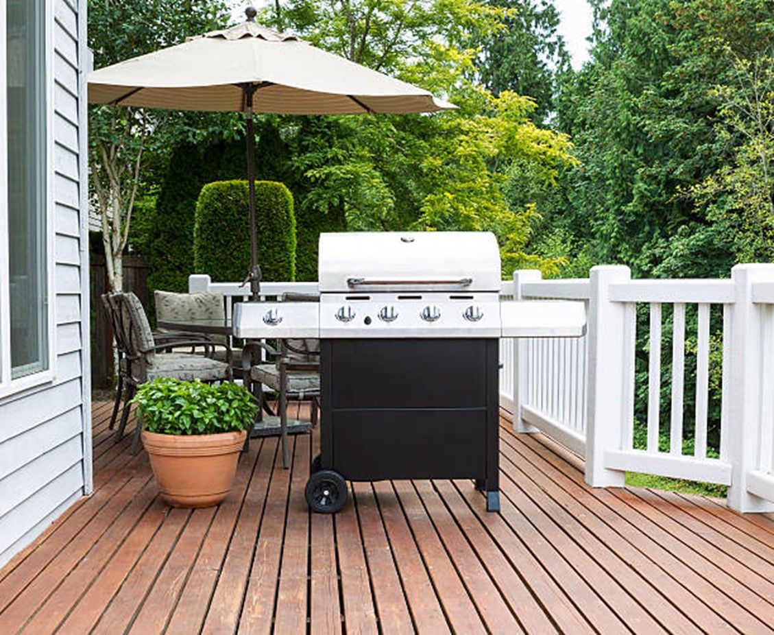 A Wooden pation with a grill and outdoor sitting area surrounded by nature.