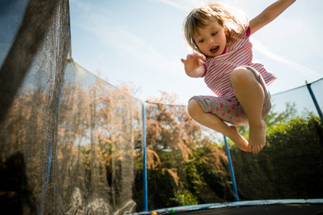 A child jumping on a tramp with trees in the background