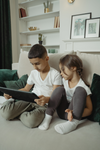 Two children sit on a couch in a living room looking at a tablet under 300